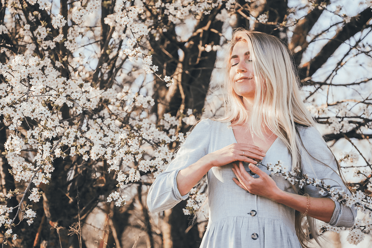 Woman in front of blossoming tree with eyes closed tapping on the side of the hand using EFT