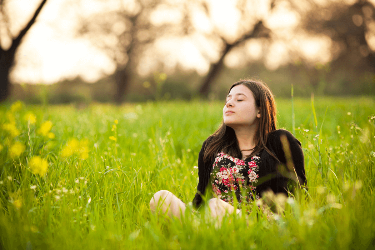 Woman sitting in field in the sun looking calm and at ease after releasing stress with Tapping