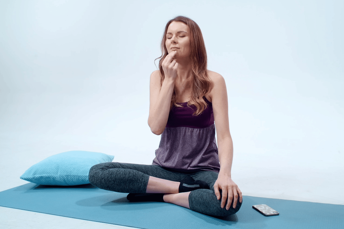 Woman sitting cross legged on yoga mat using EFT Tapping for stress relief, tapping under the chin.