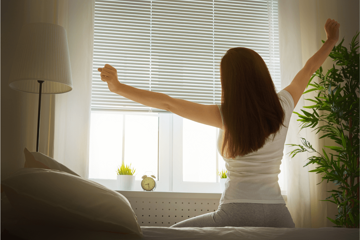 Woman sitting on bed stretching arms, waking up after sleeping well