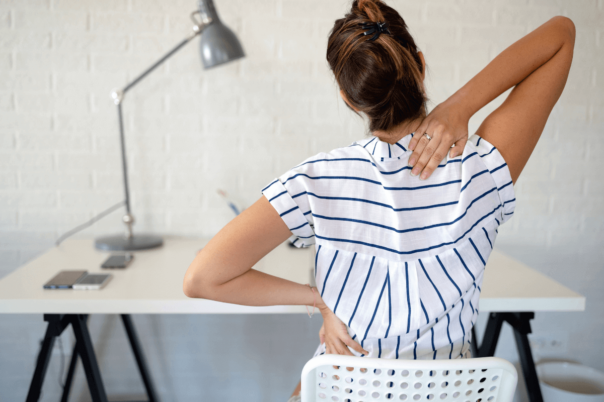 Woman with back pain at desk with arms on her back