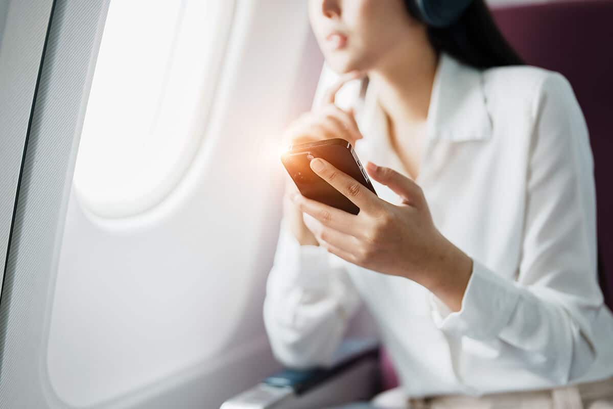Woman on airplane looking out the window, holding her phone to do an EFT Tapping meditation for fear of flying