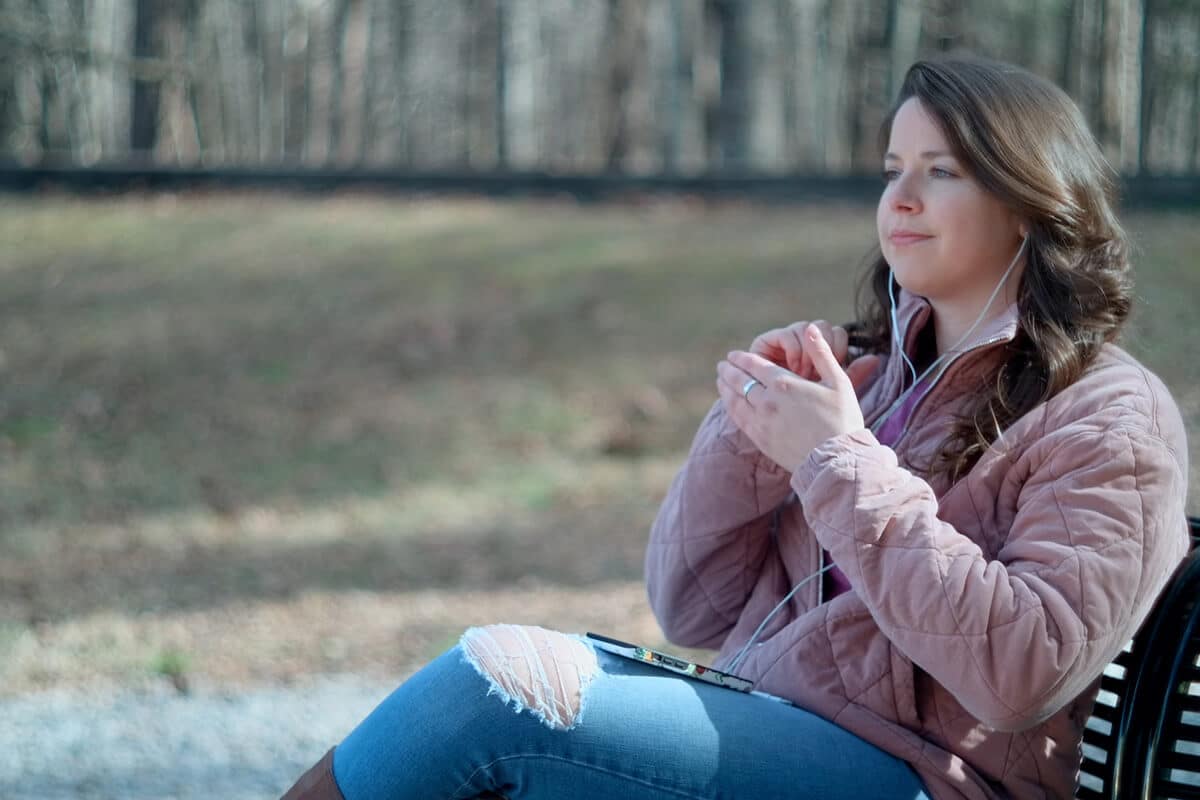 Woman on park bench doing EFT Tapping while listening to a The Tapping Solution meditation